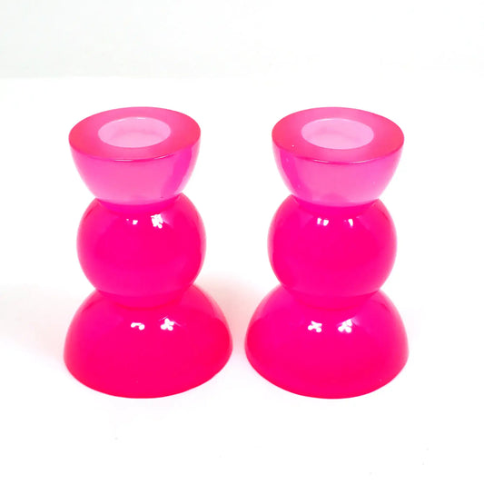 Side view of the handmade neon resin rounded geometric candlestick holders. They are bright neon pink in color. They are shaped with a semi circle at the top and bottom with a sphere shape in between.