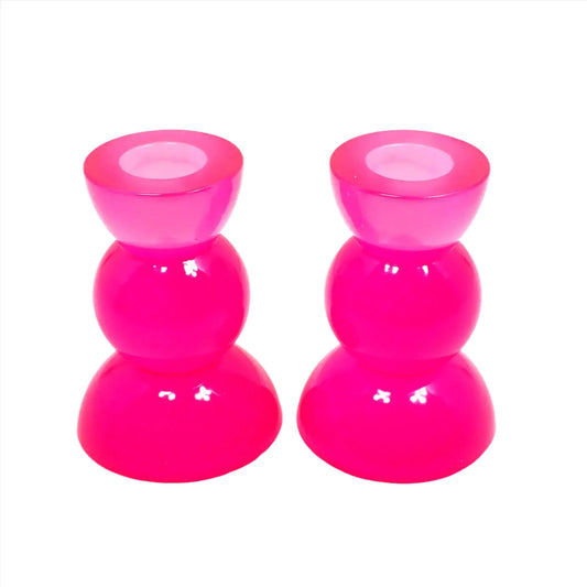 Side view of the handmade neon resin rounded geometric candlestick holders. They are bright neon pink in color. They are shaped with a semi circle at the top and bottom with a sphere shape in between.
