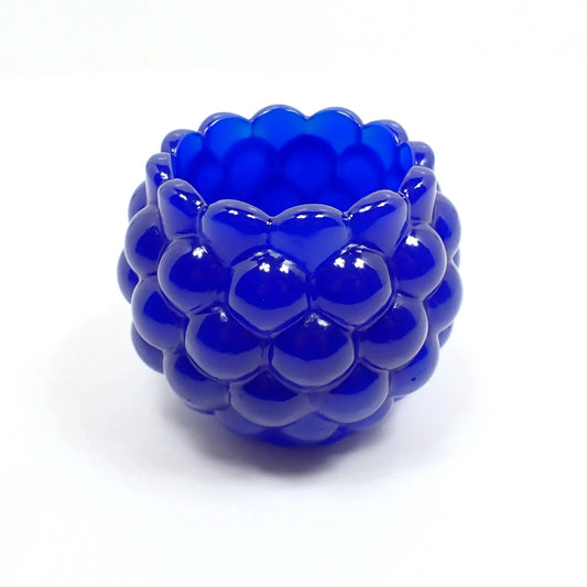 Side view of the handmade resin decorative bowl. The resin is royal blue in color and mostly opaque. It has a rounded shape with a bumpy round ball textured on the outside. The top tapers slightly and has a scalloped edge.