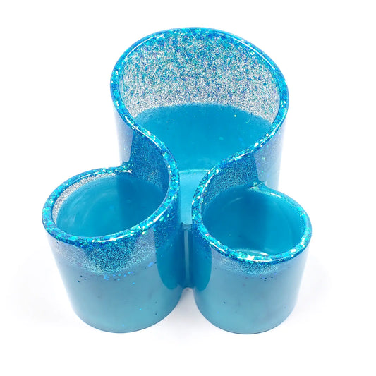 Front view of the handmade resin makeup brush holder. It has pearly light aqua blue resin with iridescent glitter at the top. There are three round areas to hold the brushes with the back having the tallest side.