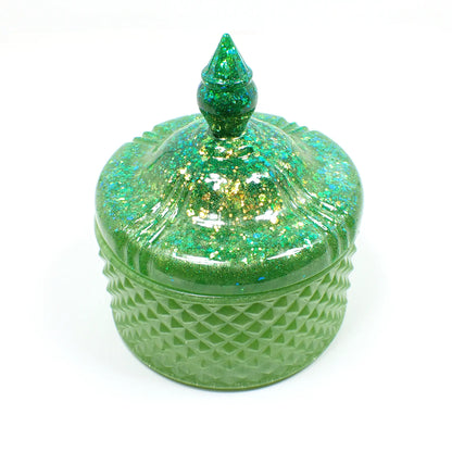 Side view of the handmade large trinket candy dish. It has pearly lime green resin with chunky iridescent glitter on the lid. It is round in shape with a textured diamond shape pattern around the sides. The top is pointed to lift the lid off. 