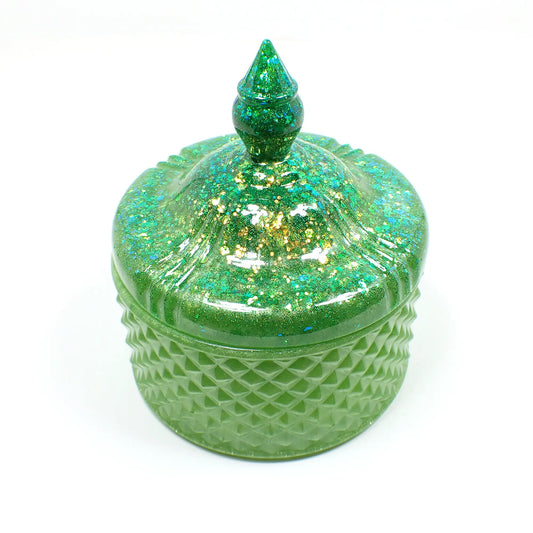 Side view of the handmade large trinket candy dish. It has pearly lime green resin with chunky iridescent glitter on the lid. It is round in shape with a textured diamond shape pattern around the sides. The top is pointed to lift the lid off. 