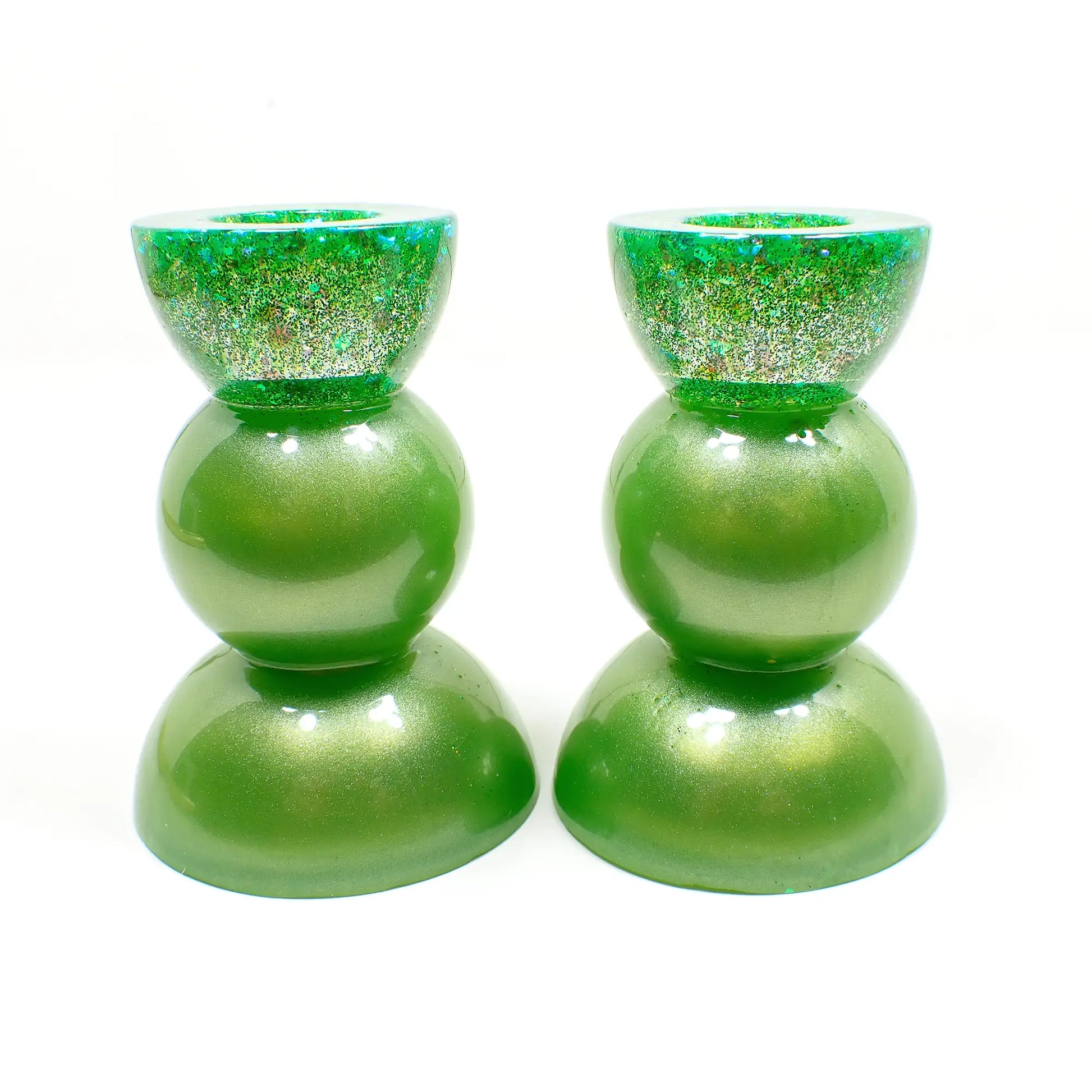 Side view of the handmade resin rounded geometric candlestick holders. They are pearly lime green in color with chunky iridescent glitter at the top. They are shaped with a semi circle at the top and bottom with a sphere shape in between. 