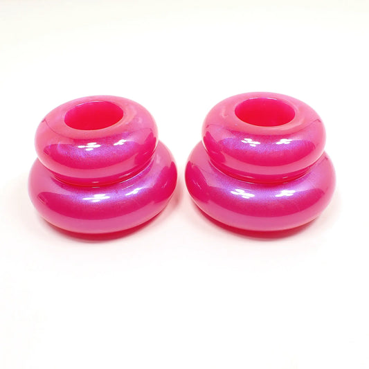Side view of the pair of handmade double ring candlestick holders. They are shaped like puffy donut rings with a larger one on bottom and a smaller one on top. The resin is bright pearly pink in color. There is a round hole at the top for the candlesticks to go in.