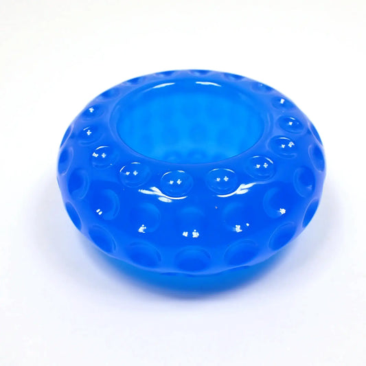 Side view of the small handmade resin succulent pot. It is short round saucer shaped with indented round dots all the way around it. There is an opening at the top for putting a succulent or tiny items. It is neon blue in color.