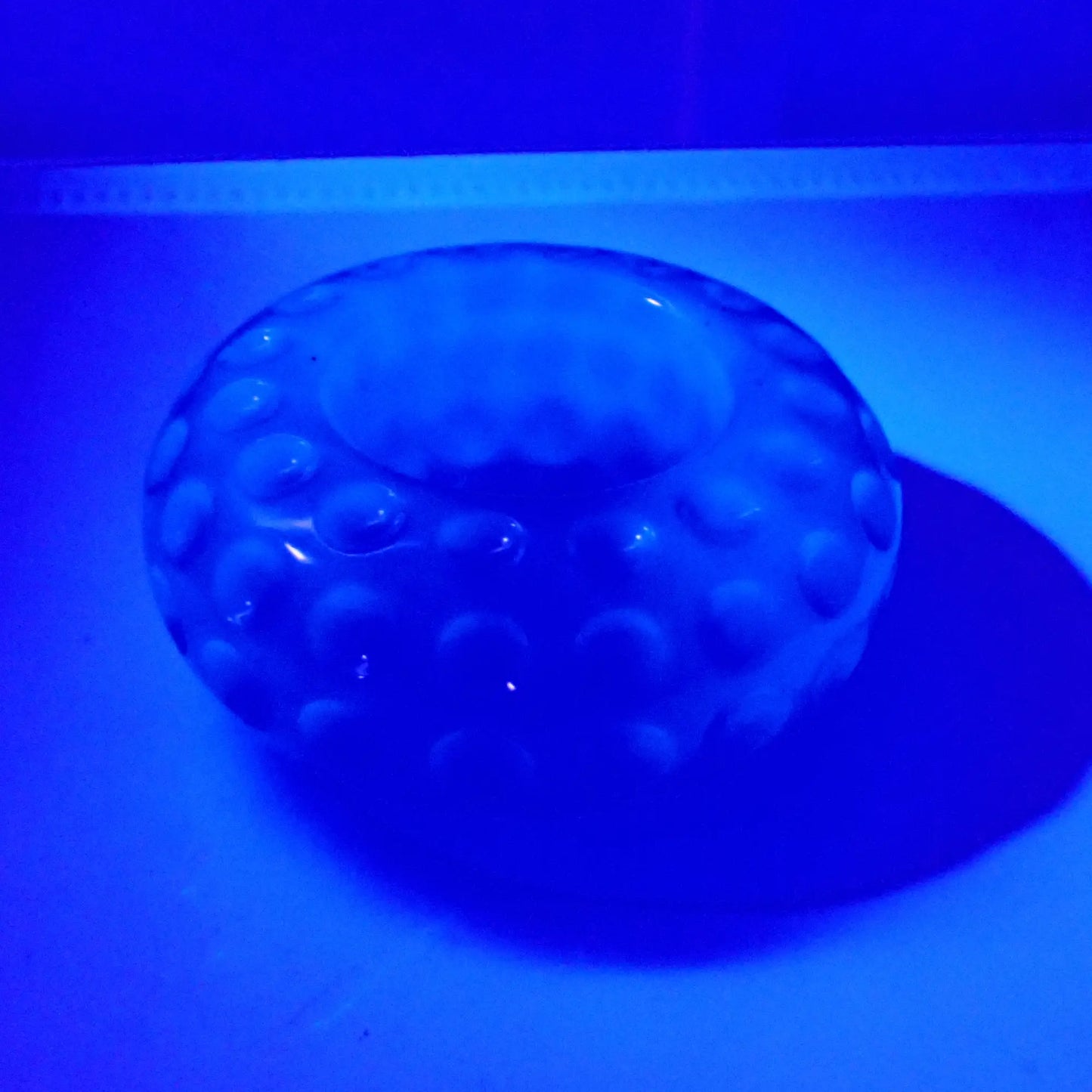 Photo of the handmade neon blue resin tealight candle holder showing how it fluoresces under a UV light.