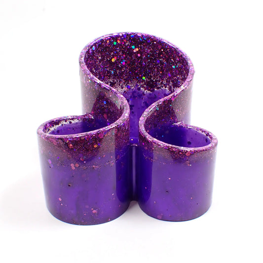 Front view of the handmade resin makeup brush holder. It has three rounded areas to hold brushes and is bright pearly purple with chunky iridescent purple glitter on top.
