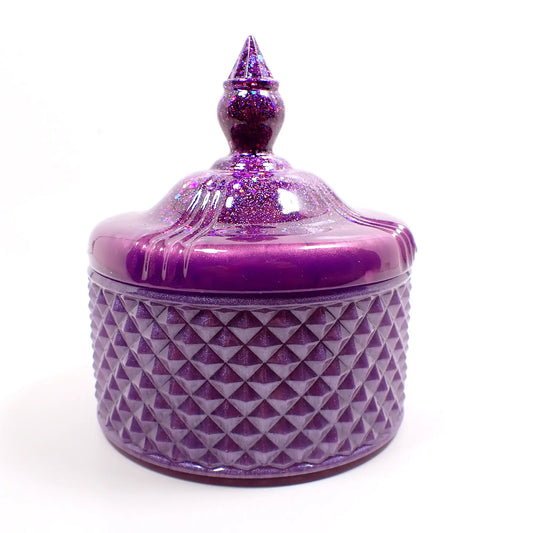 Side view of the handmade resin trinket box candy dish. The top lid has a pointed top and is bright lilac purple with chunky iridescent glitter. The bottom has a textured diamond shape pattern and is a pearly lighter shade of violet purple.