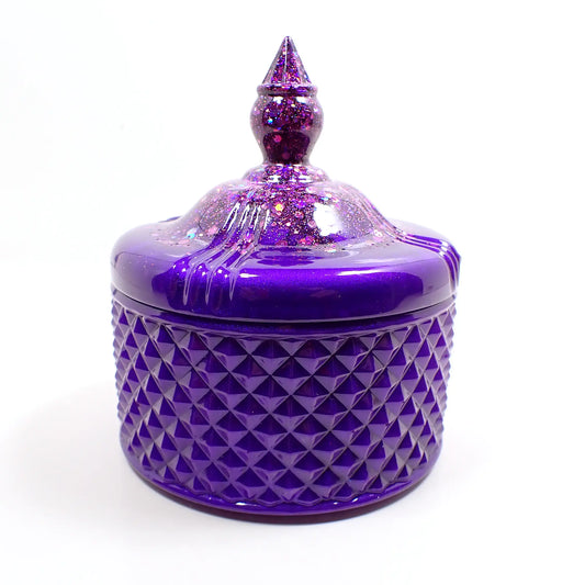 Side view of the handmade trinket box candy dish. It has a pointed top and a textured diamond shape pattern on the bottom. It is bright pearly purple resin with chunky iridescent glitter at the top.