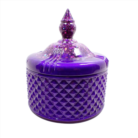 Side view of the handmade trinket box candy dish. It has a pointed top and a textured diamond shape pattern on the bottom. It is bright pearly purple resin with chunky iridescent glitter at the top.