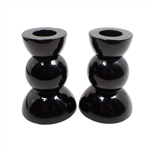 Side view of the handmade geometric candlestick holders. They have three rounded areas with a flared out top and bottom. The resin is shiny black in color.