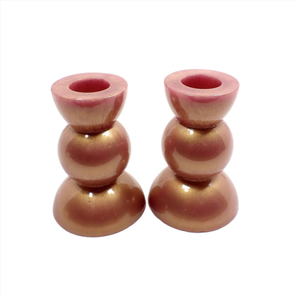 Side view of the handmade geometric candlestick holders. They have three rounded areas with a flared out top and bottom. The resin has a light color shift rose gold style with flashes of pink and light gold in color.