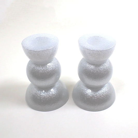 Side view of the handmade geometric candlestick holders. They have three rounded areas with a flared out top and bottom. The resin is sparkly white in color.
