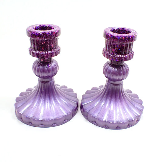 Side view of the handmade vintage style resin candlestick holders. They have light pearly purple resin on the bottom and  iridescent glitter on top. They flare out at the bottom with a corrugated appearance.