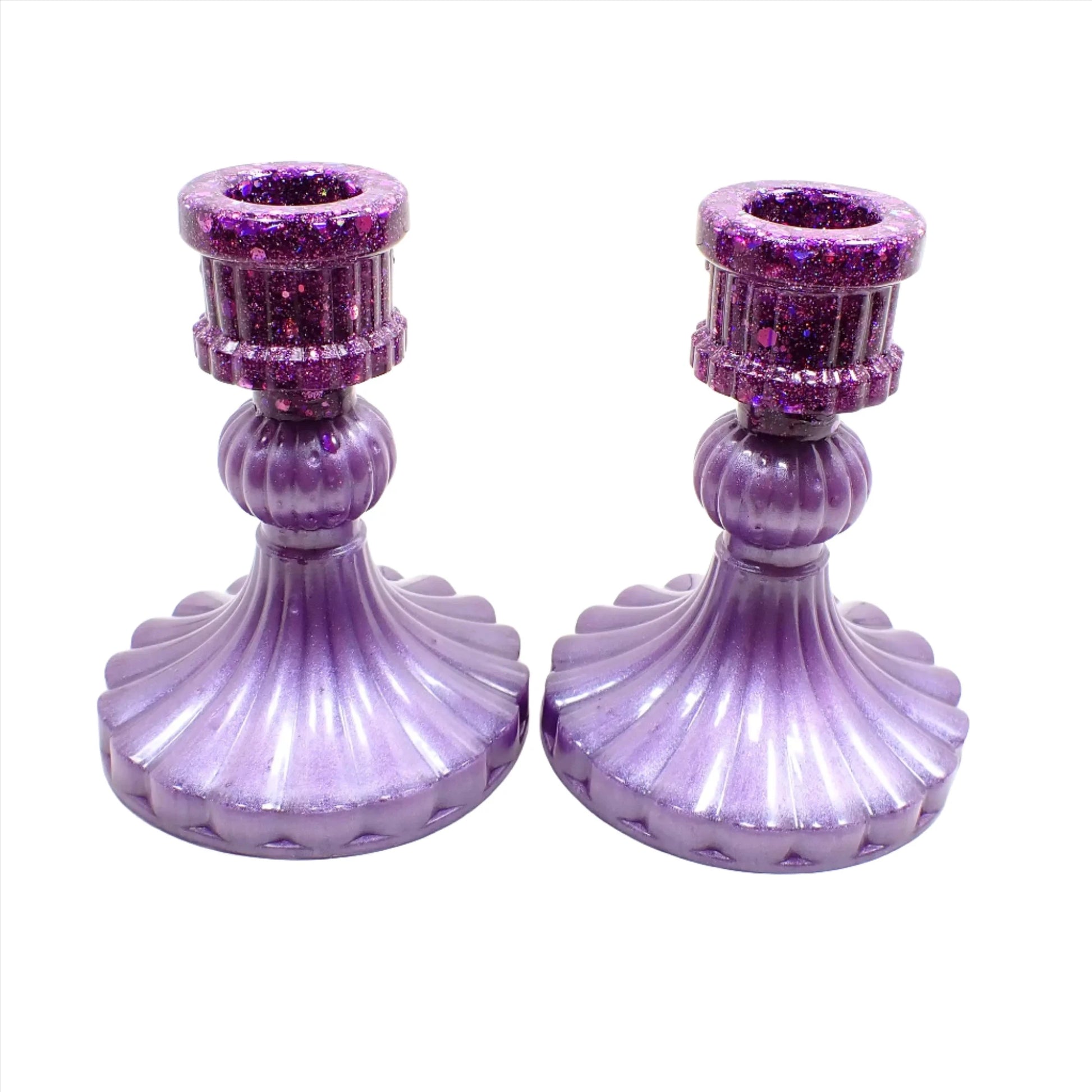 Side view of the handmade vintage style resin candlestick holders. They have light pearly purple resin on the bottom and  iridescent glitter on top. They flare out at the bottom with a corrugated appearance.