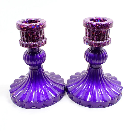 Side view of the handmade vintage style resin candlestick holders. They have bright pearly purple resin on the bottom and iridescent glitter on top. They have a corrugated ripple design with a flared out round bottom.
