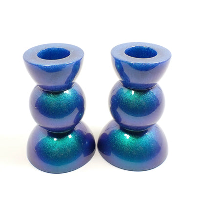 Side view of the handmade geometric candlestick holders. They have a round ball area in the middle and a semi sphere shape on the top and bottom. The resin is color shift with mostly blue to green in color with some hints of purple.