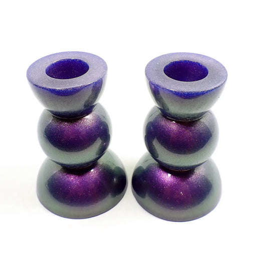Side view of the handmade geometric candlestick holders. They have a round ball area in the middle and a semi sphere shape on the top and bottom. The resin is color shift with mostly purple to green in color with some hints of blue.