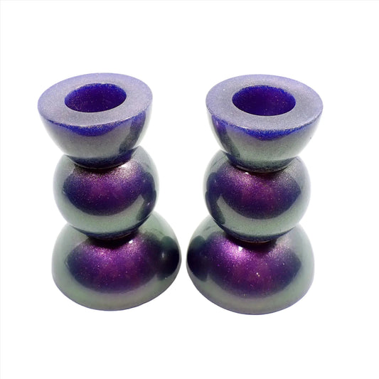 Side view of the handmade geometric candlestick holders. They have a round ball area in the middle and a semi sphere shape on the top and bottom. The resin is color shift with mostly purple to green in color with some hints of blue.