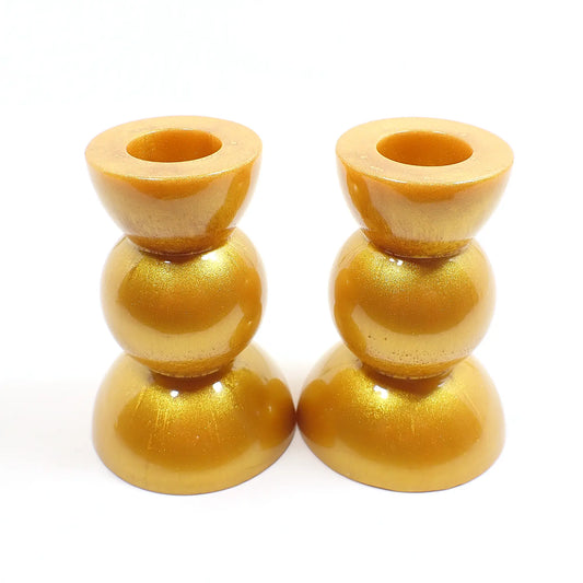 Side view of the handmade geometric candlestick holders. They have a round ball area in the middle and a semi sphere shape on the top and bottom. The resin is a rich shade of pearly metallic gold color.