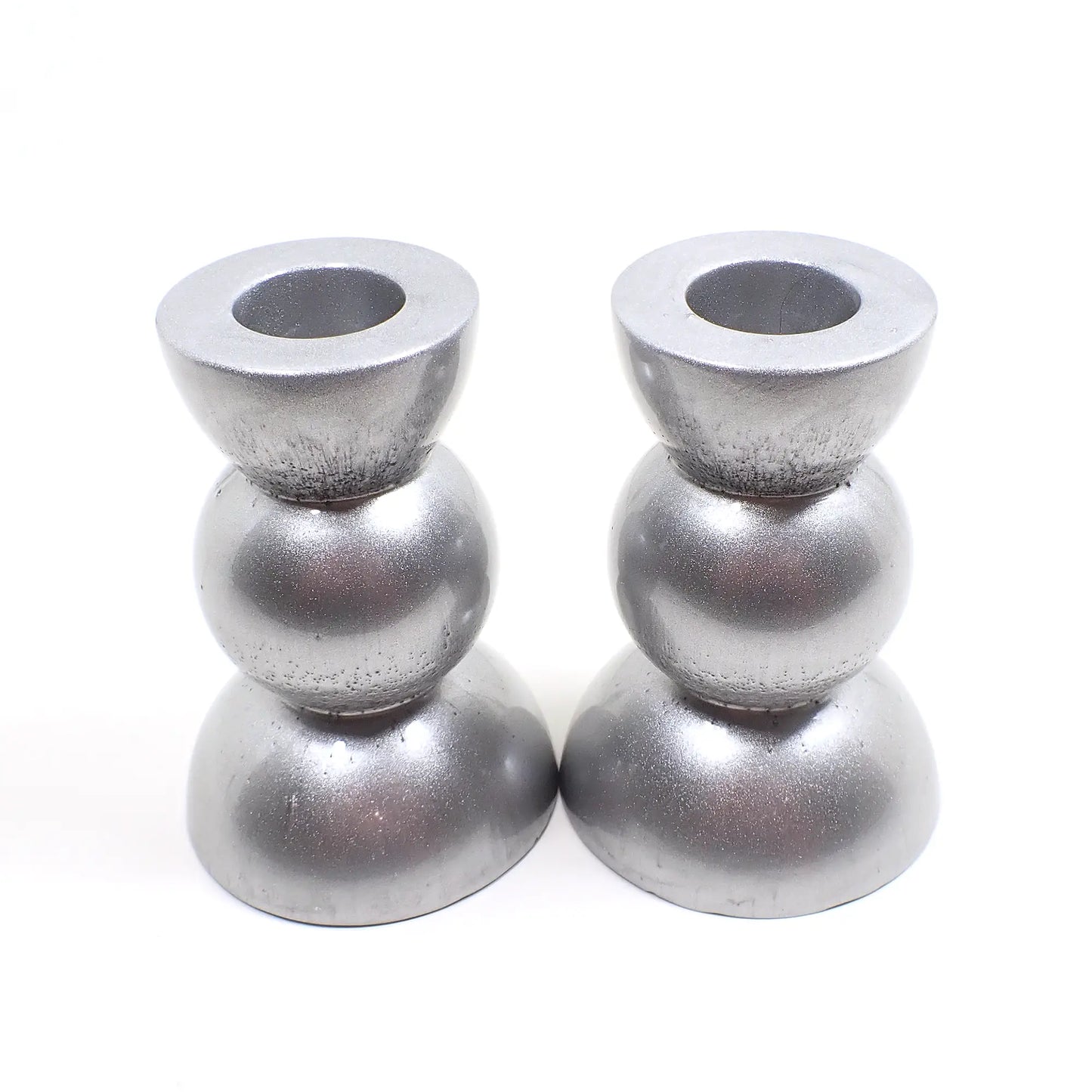 Side view of the handmade geometric candlestick holders. They have a round ball area in the middle and a semi sphere shape on the top and bottom. The resin is a rich shade of pearly metallic silver color.