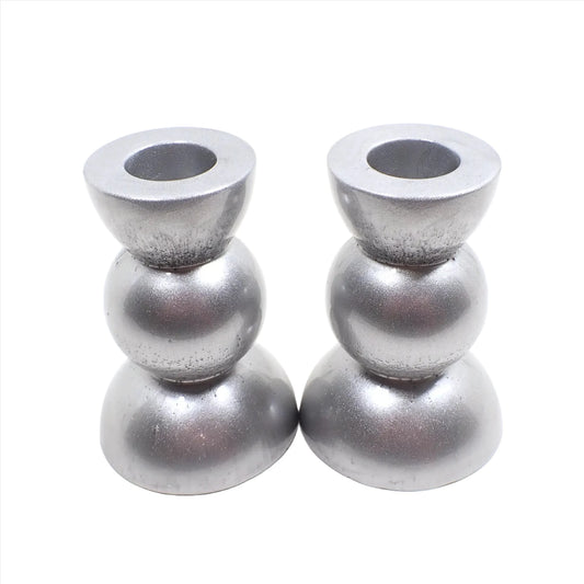 Side view of the handmade geometric candlestick holders. They have a round ball area in the middle and a semi sphere shape on the top and bottom. The resin is a rich shade of pearly metallic silver color.