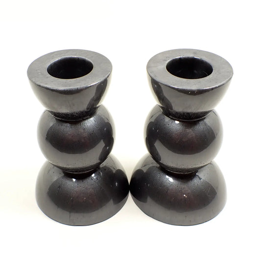 Side view of the handmade geometric candlestick holders. They have a round ball area in the middle and a semi sphere shape on the top and bottom. The resin is a dark pearly metallic gunmetal gray color.