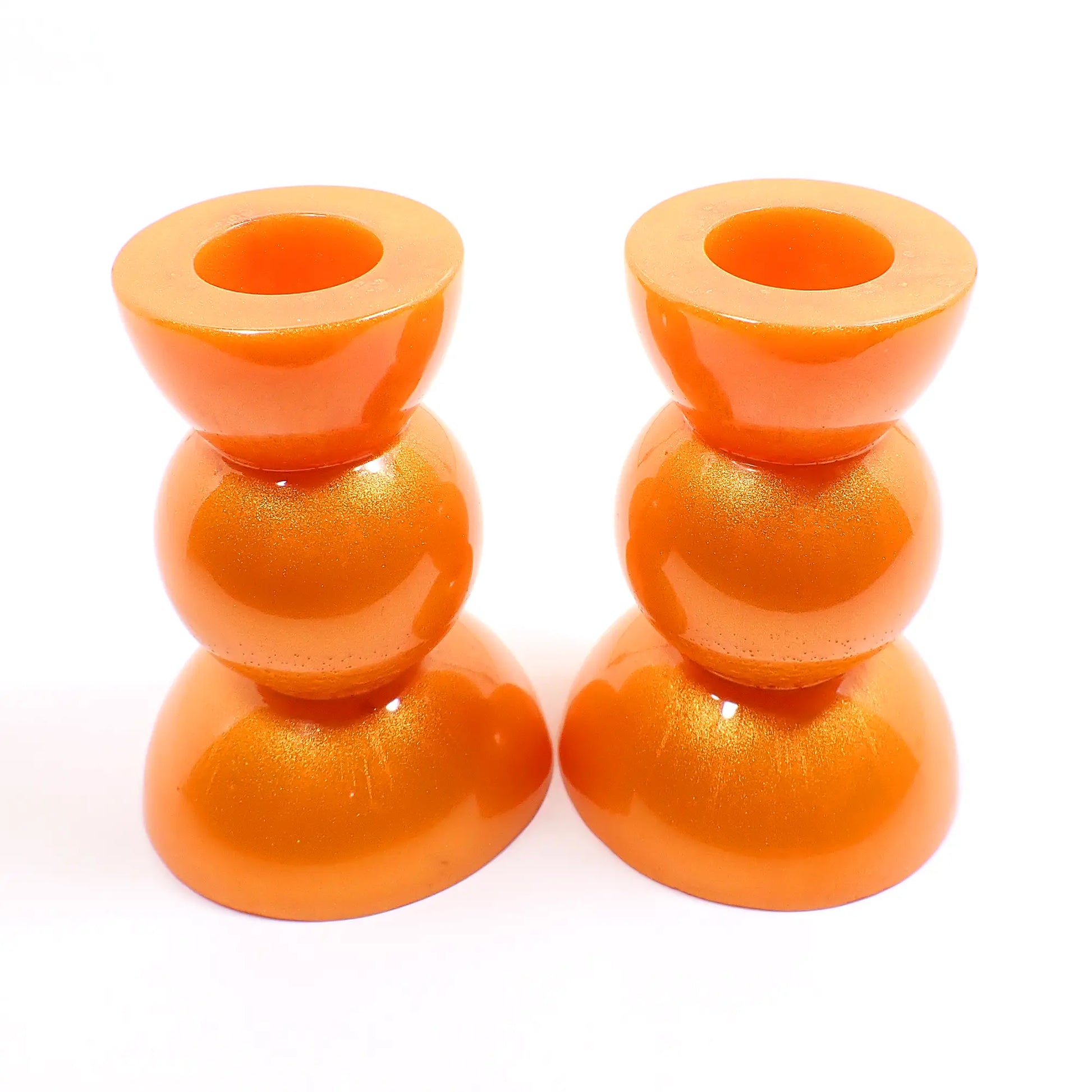 Side view of the handmade geometric candlestick holders. They have a round ball area in the middle and a semi sphere shape on the top and bottom. The resin is a bright citrus orange color with hints of metallic gold.