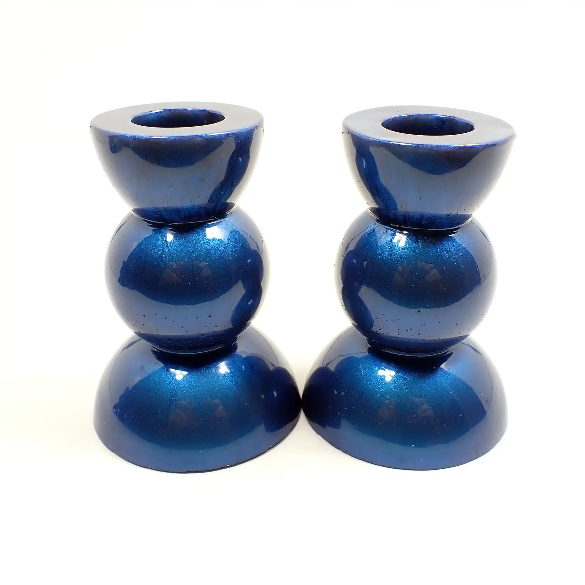 Side view of the handmade geometric candlestick holders. They have a round ball area in the middle and a semi sphere shape on the top and bottom. The resin is a pearly deep blue color.