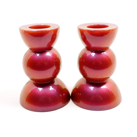 Side view of the handmade geometric candlestick holders. They have a round ball area in the middle and a semi sphere shape on the top and bottom. The resin is a pearly color shift resin with red, orange, pink, and purple hues like a sunset.