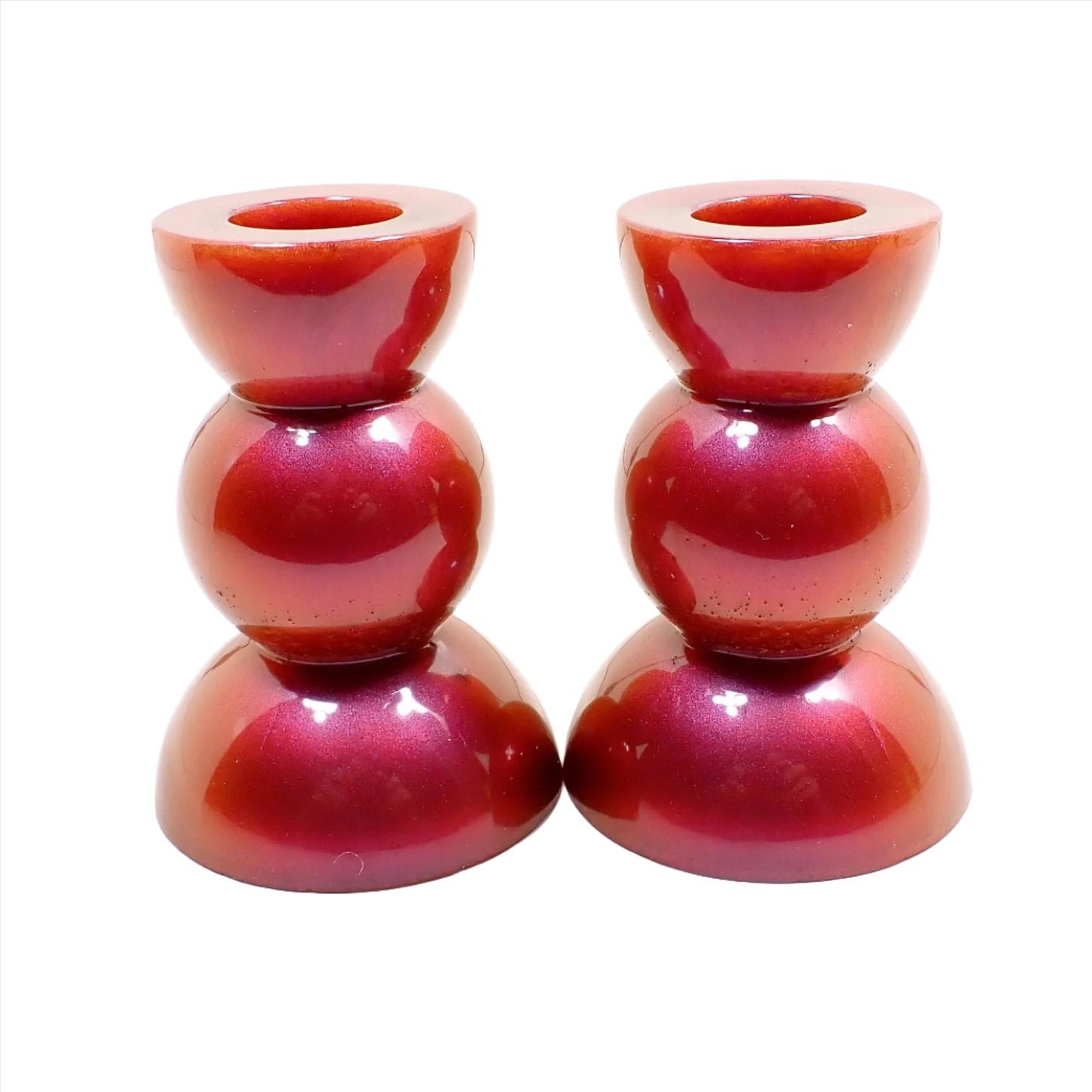 Side view of the handmade geometric candlestick holders. They have a round ball area in the middle and a semi sphere shape on the top and bottom. The resin is a pearly color shift resin with red, orange, pink, and purple hues like a sunset.
