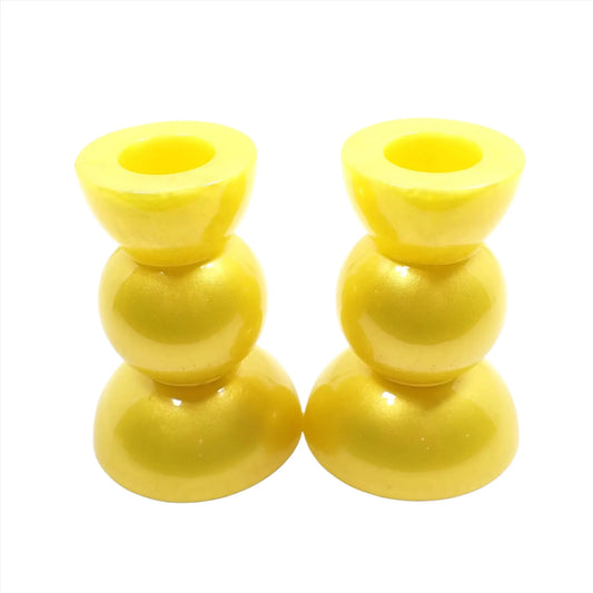 Side view of the handmade geometric candlestick holders. They have a round ball area in the middle and a semi sphere shape on the top and bottom. The resin is a bright pearly yellow color.