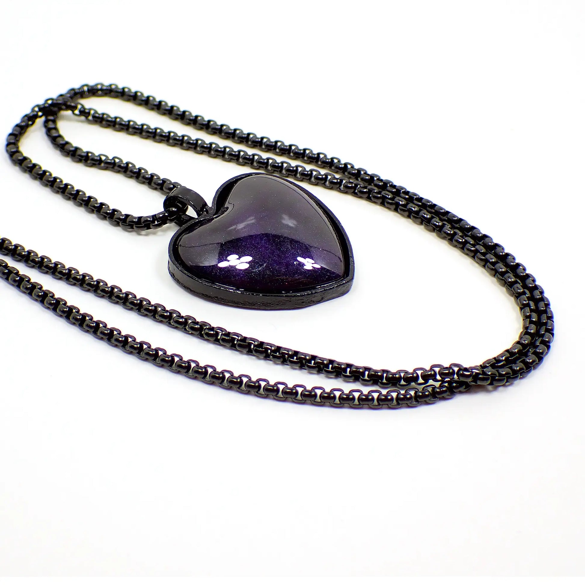 enlarged view of the Goth handmade resin heart pendant necklace. The box chain and pendant setting are black coated in color. The pendant is shaped like a heart with pearly black resin that has dark pearly blue with hints of purple mixed in.