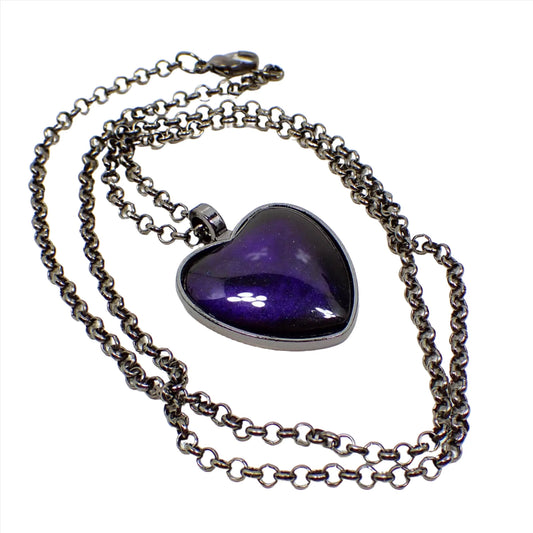 Enlarged image of the handmade resin Goth heart pendant necklace. The metal is gunmetal gray in color. The chain has a round link rolo chain design with a lobster claw clasp showing at the end. The heart pendant has dark pearly black resin with areas of dark pearly blue mixed in that has some hints of purple.