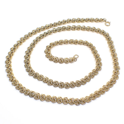 Top view of the retro vintage chain necklace. It is a darker gold tone in color with a spring ring clasp at the end. The links have several round links set together to form a round pinwheel like design.