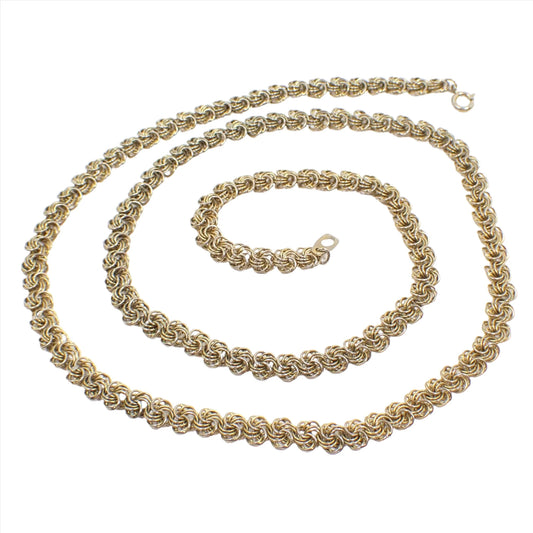 Top view of the retro vintage chain necklace. It is a darker gold tone in color with a spring ring clasp at the end. The links have several round links set together to form a round pinwheel like design.