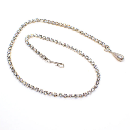 Photo showing the Mid Century vintage Coro choker necklace. The metal is silver tone in color. There is a single strand of small clear round rhinestones. The end has a chain and the other side has a hook clasp.