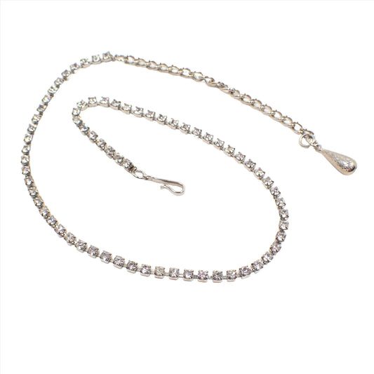 Photo showing the Mid Century vintage Coro choker necklace. The metal is silver tone in color. There is a single strand of small clear round rhinestones. The end has a chain and the other side has a hook clasp.