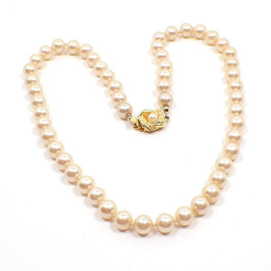 Top view of the retro vintage Talbots faux pearl necklace. The glass imitation pearl beads are an off white golden color. They are potato shaped and are hand knotted between each bead. There is a gold tone box clasp at the end with a braided knot design with a faux pearl in the middle.