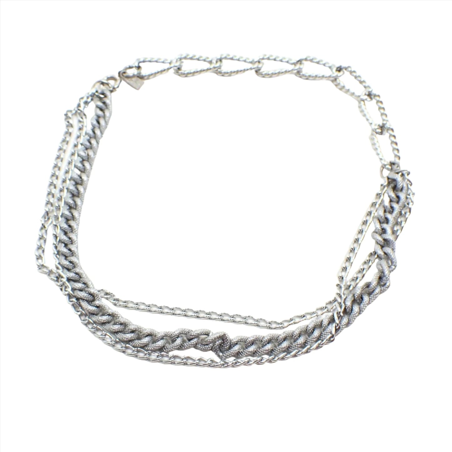 Top view of the retro vintage Emmons multi strand chain necklace. The metal is silver tone in color and has a spring ring clasp at the end. Part of the necklace has larger sized textured oval curb links and the other part has three strands of small sized link chains. Two of the three strands are shiny and the other is slightly bigger with textured links.