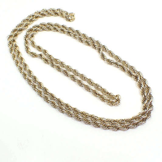 Top view of the retro vintage Monet chain necklace. It has silver and gold tone color on each link. The chain has a wide twisted rope design. There is a spring ring clasp at the end with a hang tag for Monet.