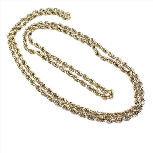 Top view of the retro vintage Monet chain necklace. It has silver and gold tone color on each link. The chain has a wide twisted rope design. There is a spring ring clasp at the end with a hang tag for Monet.
