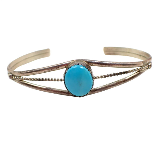 Front view of the retro vintage faux turquoise cuff bracelet. The metal is silver tone in color. It has an open front design with a twisted wire area in the middle.  The front has an oval glass cab made to look like turquoise. 