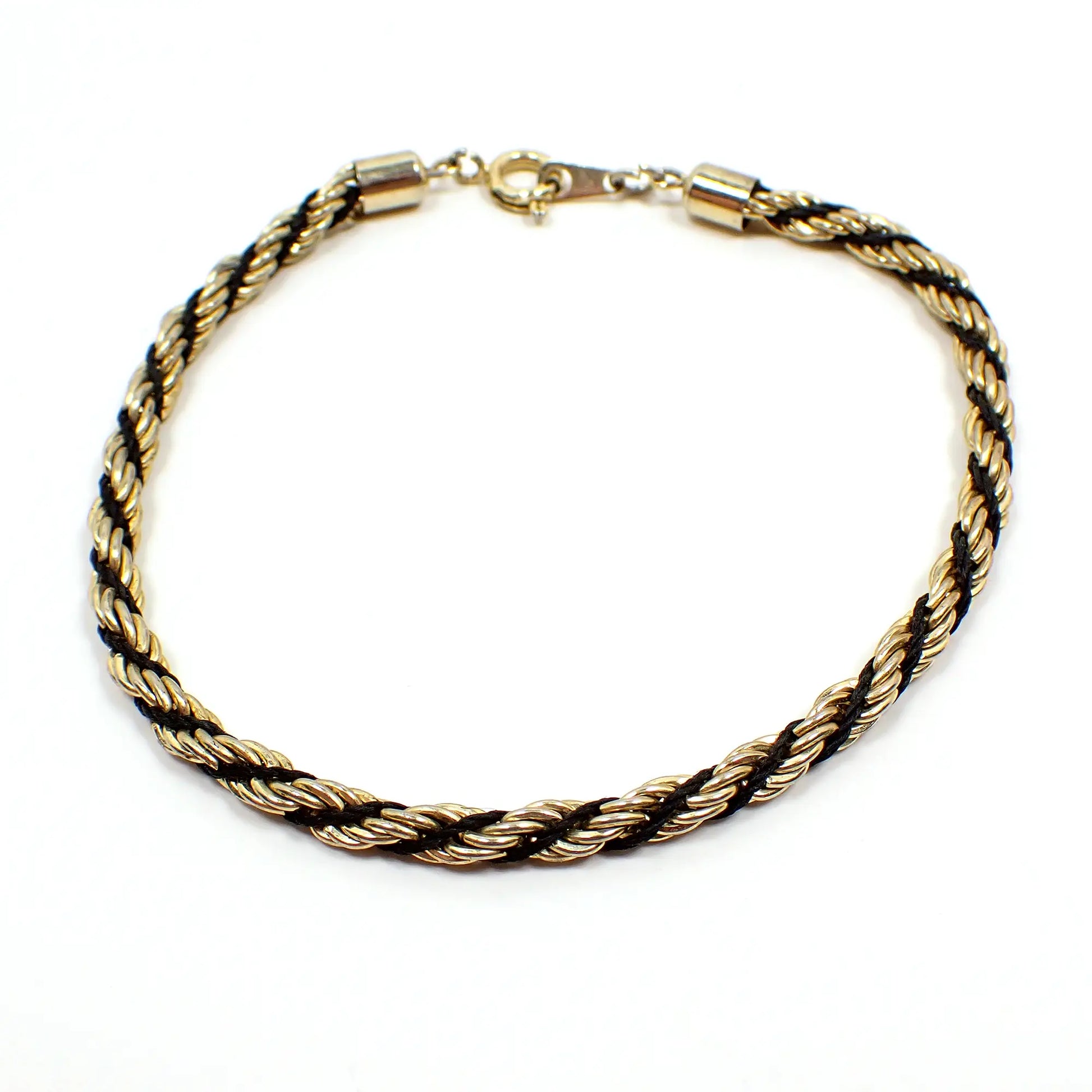 Top view of the retro vintage twisted rope chain bracelet. The metal is gold tone in color. It has a twisted design with black stringing material and a spring ring clasp at the end.