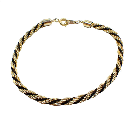Top view of the retro vintage twisted rope chain bracelet. The metal is gold tone in color. It has a twisted design with black stringing material and a spring ring clasp at the end.