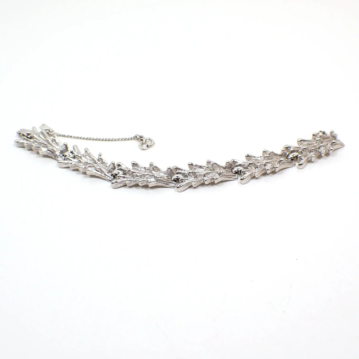 Angled view of the Mid Century vintage Monet link bracelet. The metal is textured matte silver tone in color. The links have a rounded end spiky Brutalist style appearance. There is a snap lock clasp at the end and a safety chain with hinged clasp. 