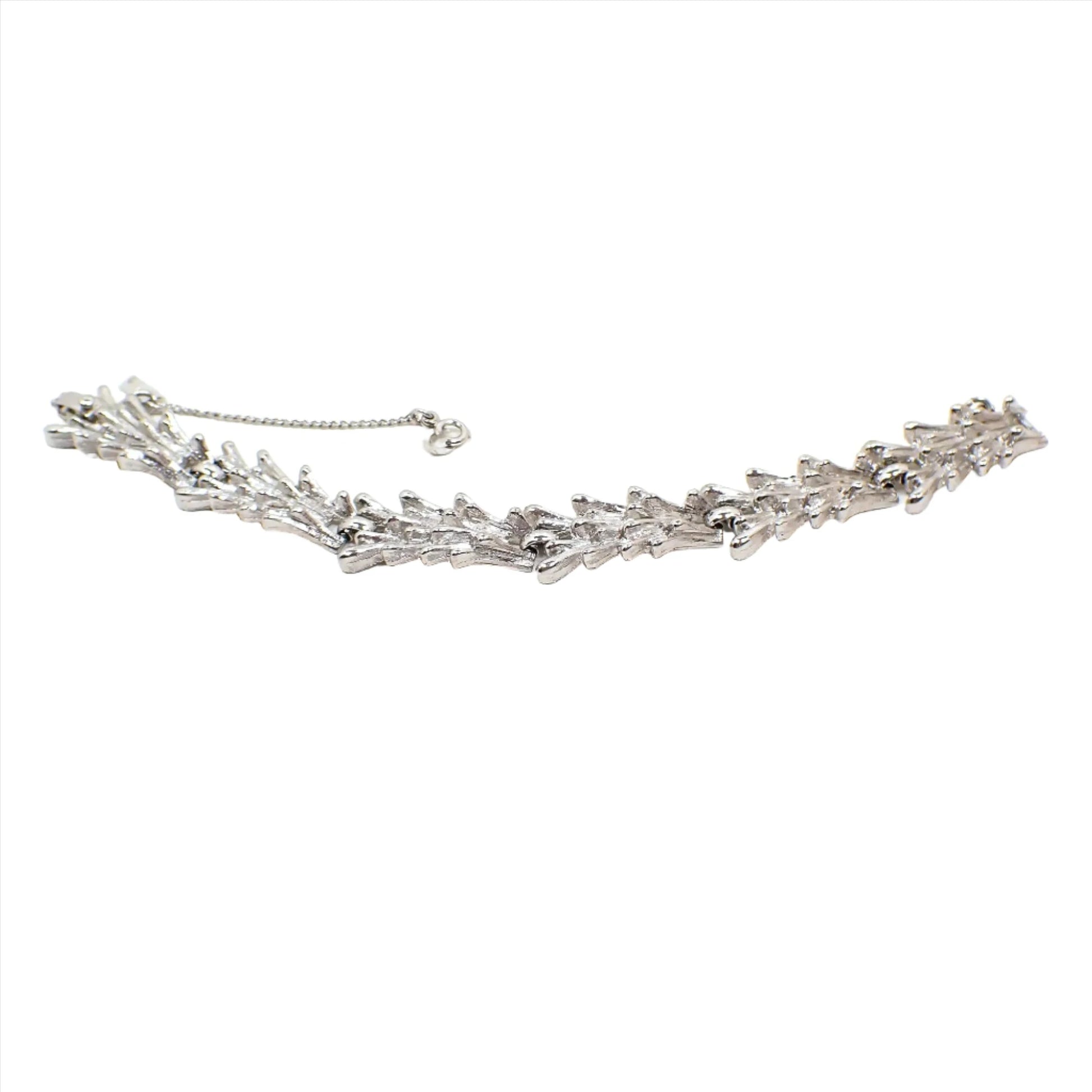 Angled view of the Mid Century vintage Monet link bracelet. The metal is textured matte silver tone in color. The links have a rounded end spiky Brutalist style appearance. There is a snap lock clasp at the end and a safety chain with hinged clasp. 