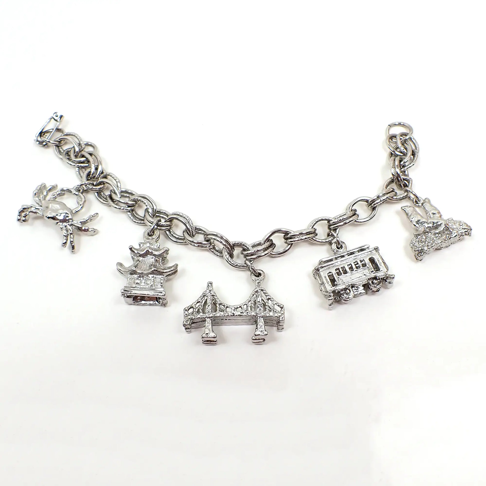 Side view of the retro vintage San Francisco charm bracelet. It's silver tone in color with a snap lock clasp. There are charms for a crab, China Town, Golden Gate Bride, cable car, and seals.