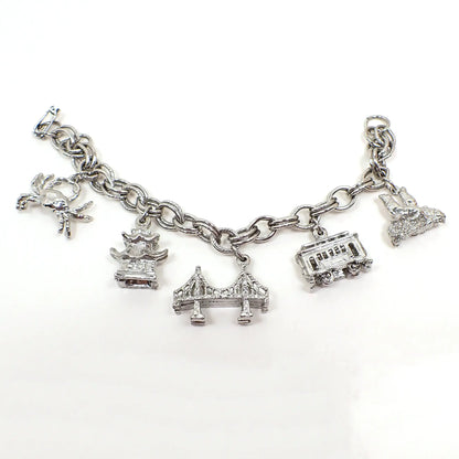 Side view of the retro vintage San Francisco charm bracelet. It's silver tone in color with a snap lock clasp. There are charms for a crab, China Town, Golden Gate Bride, cable car, and seals.