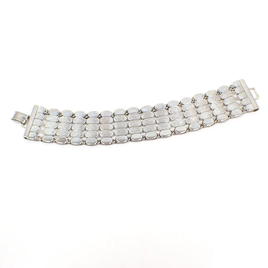 Top view of the wide Mid Century vintage link bracelet. The metal is silver tone in color. There are five rows of small oval links. The outer rows are shiny and the inner ones have a textured matte appearance. There is a snap lock clasp at the end.